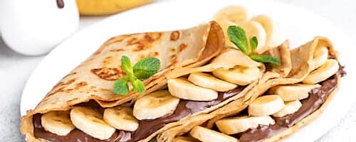 Crepes stuffed with chocolate spread and banana on white plate. Thin pancakes, blini. Sweet dessert.